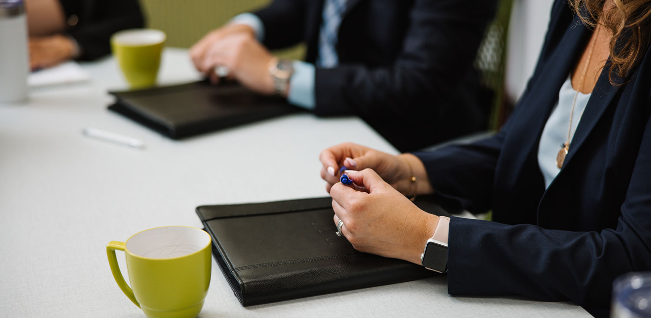 Woman holding pen over a portfolio sitting at a conference room table.